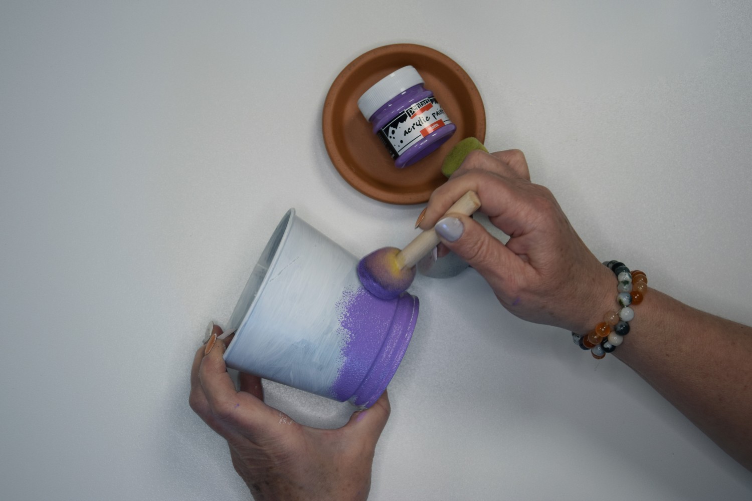 Žena nanáša fialovú vrstvu akrylovej farby na podklad tupovacím štetcom.